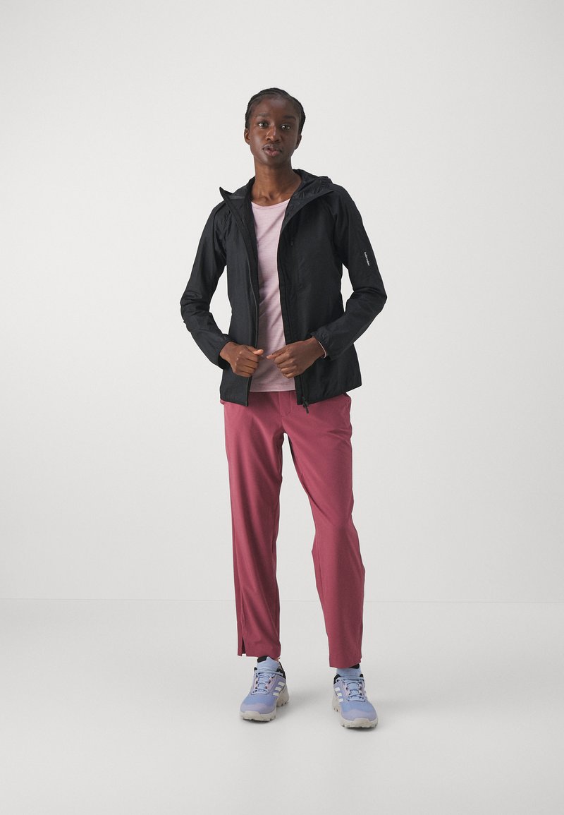 Schwarze leichte Jacke mit Kapuze, kombiniert mit einem rosa Oberteil und bordeauxrotfarbenen Hosen. Die Schuhe sind hellblau mit einer strukturierten Sohle.