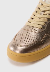 Sneaker in bronzo metallico con punta perforata, lacci beige e suola in gomma. Caratterizzato da una texture liscia e design a punta rotonda.