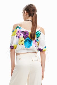 Blomstret off-shoulder crop top i hvid, med livlige lilla, gule og blå mønstre. Indsnævret talje med snore, korte ærmer.