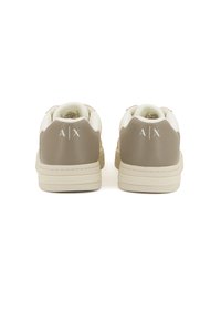 Zapatillas beige y crema con un acabado texturizado, suelas planas y un logo "A/X" en el talón. Parte superior de cuero y cuello acolchado para mayor comodidad.