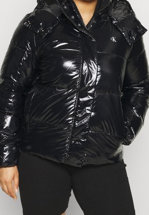 Doudoune noire en matériau brillant, dotée d'une fermeture à zip et à boutons pression, avec des poches à rabat et une capuche. Logo Calvin Klein sur la poitrine.