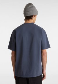 Herrblå bomullströja med kort ärm och rund hals, sedd bakifrån, i kombination med en grå mössa. Minimalistisk design, mjuk textur.