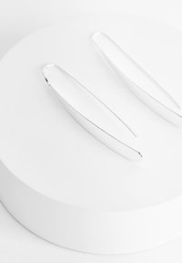 Boucles d'oreilles allongées en argent au design élégant, présentant une texture lisse et un éclat subtil, exposées sur un piédestal circulaire blanc.