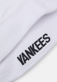 Calcetines de algodón blancos con un logo bordado en negro que dice "YANKEES" en el lateral, con una textura suave y grosor medio.