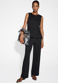 Top noir sans manches en peplum associé à un pantalon noir ajusté, complété par un sac à main argenté froissé et des sandales noires à lanières.