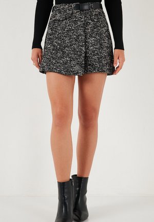 Black and white tweed skirt with pleats, a belted waist, and subtle texture. Paired with black ankle boots and a long-sleeve top.