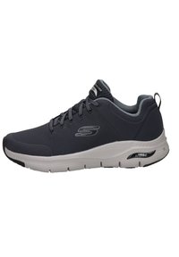 Zapatilla deportiva con una parte superior de malla gris, detalles en gris claro y una suela blanca. Cuenta con un acolchado en el cuello y una lengüeta trasera para ponerlas fácilmente.