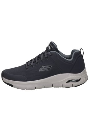 Zapatilla deportiva con una parte superior de malla gris, detalles en gris claro y una suela blanca. Cuenta con un acolchado en el cuello y una lengüeta trasera para ponerlas fácilmente.