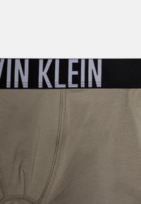 Sivé bavlnené slipy s čiernym elastickým pásom, na ktorom je nápis "CALVIN KLEIN" v kontrastnej bielej farbe, s hladkou textúrou.