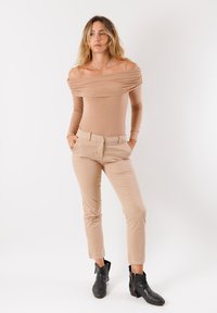 Body beige scollato con maniche lunghe, abbinato a pantaloni beige su misura. Stivaletti neri alla caviglia con dettagli in zip. Tessuto dalla consistenza liscia.