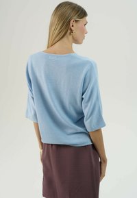 Svetlomodrý sveter s voľným strihom, širokými trojštvrťovými rukávmi a okrúhlym výstrihom, doplnený o tmavofialovú sukňu.