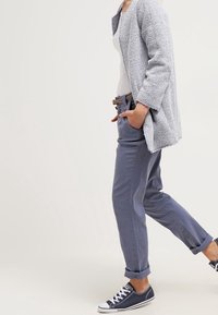 Ljusgrå, strukturerad cardigan över en vit topp, i kombination med uppvikta blå byxor och marinblå sneakers. Enkelt designad med en avslappnad passform.