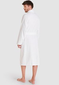 Bata de baño de toalla blanca con mangas largas, cuello de chal y cinturón atado a la cintura, con una tela texturizada y diseño hasta la rodilla.