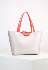 Srebrna torba tote o teksturowanym wykończeniu, z koralowymi ramiączkami i pasującą klapką zamykającą. Złoty akcent z logo blisko góry.