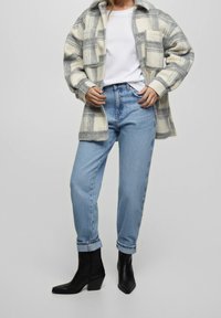 Geruite shirtjas van wolmix in grijs en crème; witte t-shirt, lichtblauwe hooggetailleerde jeans en zwarte enkellaarsjes met hak.