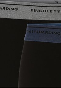 Zwarte leggings met contrasterende taillebandkleuren; de ene is grijs, de andere blauw. Beide hebben zwart bedrukte merknamen. Glad van textuur.