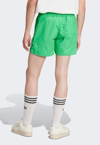 Πράσινα μαγιό με ελαστική μέση, πλευρικές τσέπες και πίσω τσέπη. Συνδυασμένα με λευκές κάλτσες με μαύρες ρίγες και κρέμ παπούτσια.