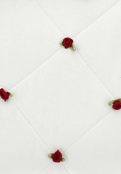Cuscino in tessuto bianco con cuciture a diamante, impreziosito da piccoli decori di rose rosse e inserti in nastro verde disposti uniformemente sulla superficie.