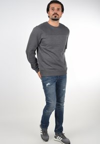 Grå hettegenser med teksturert brystpanel, brukt med blå slitte jeans og grå sneakers med hvite detaljer. Uformell passform.