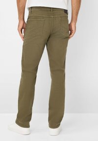 Pantaloni verde oliva con un design a gamba dritta, due tasche posteriori e una trama sottile. Abbinati a sneaker bianche.