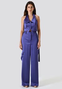 Lila Satin-Haltertop mit Knöpfen, Ausschnitt in der Taille, kombiniert mit passenden weiten Hosen mit Cargo-Taschen und seitlichen Schnüren.