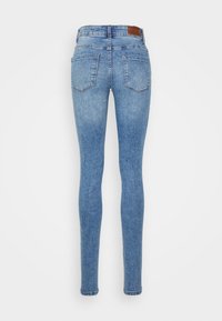 Jeans skinny em denim azul claro, com uma cintura média, mínimas desgastes, dois bolsos traseiros e um retângulo de couro castanho na cintura.