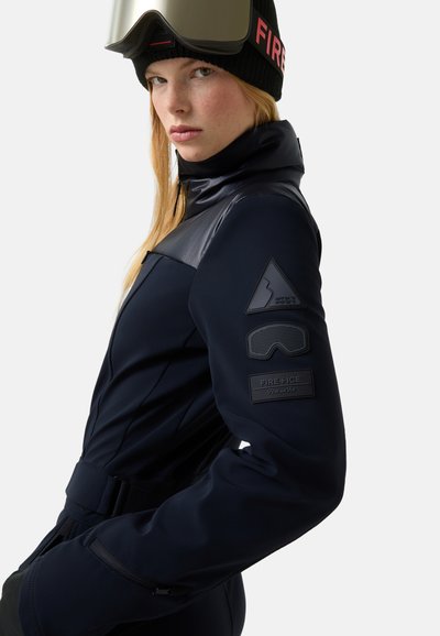 Tmavě modrý lyžařský oblek s vysokým límcem, strukturovanými ramenními panely a značkovými nášivkami na rukávech. Má přiléhavý střih a nastavitelný pas.