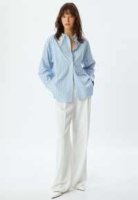 Blauw-wit gestreepte oversized button-up shirt met een kantafgewerkte kraag, gecombineerd met witte wijde broekspijpen en schoenen met puntige neuzen.
