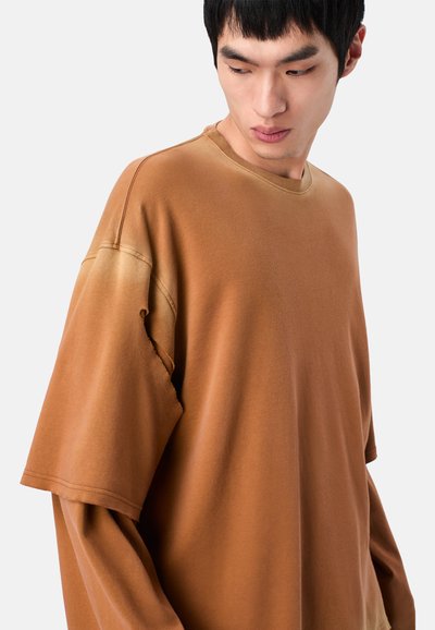 Braunes, übergroßes T-Shirt mit einem Farbverlaufseffekt, aus weichem Stoff hergestellt. Verfügt über einen ausgefransten Ärmel und einen Rundhalsausschnitt.