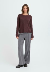 Pull en maille bordeaux à manches longues et design texturé, associé à un pantalon gris à jambes larges et des chaussures noires. Tenue simple et décontractée.