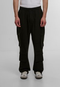 Svarte cargo bukser med elastisk midje, flere side lommer og avslappet passform, laget av myk stoff, paret med hvite sneakers.