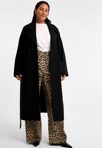 Zwarte lange jas met grote kraag en knopen aan de voorkant, gecombineerd met wijde broek met luipaardprint. Gladde textuur, oversized pasvorm, minimalistisch design.