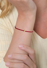 Bracelet en cordon rouge avec un petit pendentif en forme d'étoile dorée. Le cordon est lisse, et l'étoile présente un design à cinq pointes, offrant une apparence délicate.