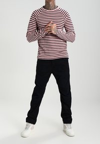 Camisa de rayas de manga larga en rosa claro y marrón oscuro, combinada con pantalones oscuros y zapatillas blancas con acentos rosas.