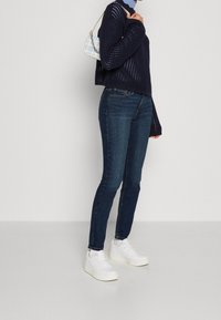 Marinblå stickad tröja med öppen väv, matchad med mörkblå slim fit jeans och vita plattformssneakers. Accessoriserad med en ljusblå väska.