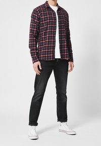 Geruit flanellen overhemd in marineblauw, rood en wit; met lange mouwen en knoopsluiting aan de voorkant. Zwarte jeans en witte hoge sneakers maken de outfit compleet.