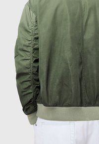 Olive green bomber jacket with ribbed cuffs and hem. Features ruching along sleeve seams and a smooth, textured fabric.