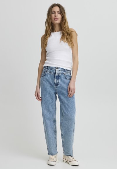 Gai zila džinsu bikses ar brīvu piegriezumu, kas iezīmē augstu jostu, klasisko piecu kabatu dizainu un pamanāmām šuvēm. Apvienotas ar baltu topiņu.