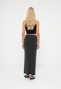 Black denim maxi skirt with two back pockets, straight cut, and a slightly faded finish, paired with a fitted black cropped top.