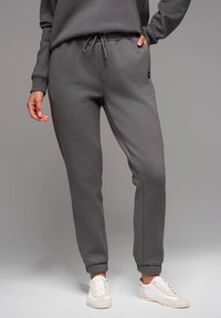 Grau Jogginghosen aus weichem, dehnbarem Stoff mit einem elastischen Bund, gerippten Säumen und seitlichen Taschen. Kombiniert mit weißen Schuhen.