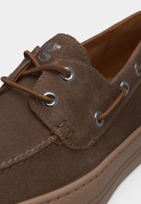 Καφέ καστόρινο ναυτικό παπούτσι με δερμάτινα κορδόνια περνώντας από μεταλλικά τρύπες και ταμπά λαστιχένια σόλα.