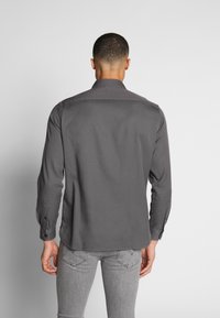 Grå långärmad skjorta med knäppt krage och kontrasterande manschettdetalj. Slät tyg, figursydd design och en böjd nederkant.