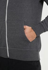 Sudadera gris con cremallera frontal, hecha de tela suave, con bolsillos laterales y diseño liso con puños acanalados.