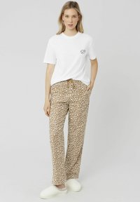 T-shirt en coton blanc avec un petit graphisme noir, associé à un pantalon imprimé léopard marron avec taille à cordon de serrage et poches latérales. Chaussures blanches à enfiler.