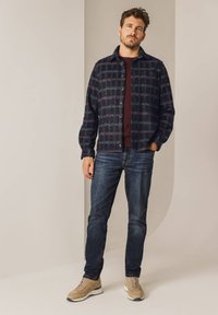 Zwart en marineblauw geruit shirtjack met knoopsluiting, gecombineerd met een bordeauxrood top, donkere denim jeans en beige sneakers.