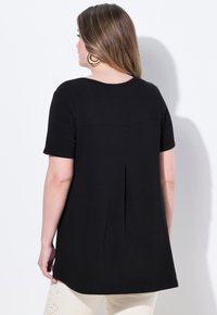 Top nero a maniche corte con vestibilità relax, caratterizzato da una piega sul retro e un collo rotondo. Tessuto morbido e testurizzato.