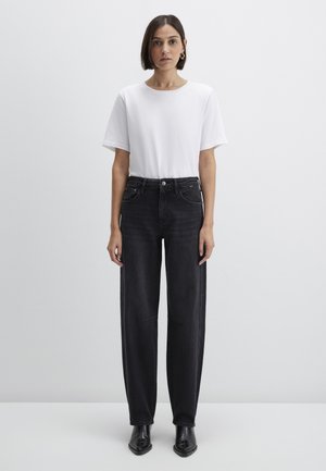 Black straight-leg jeans paired with a plain white t-shirt. The jeans have five pockets and a subtle wash detail, with black ankle boots.