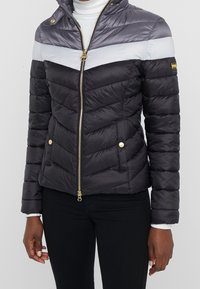 Quilted puffer jacket in dark gray, featuring a horizontal light gray stripe. Gold zipper and buttons, with a stand-up collar.