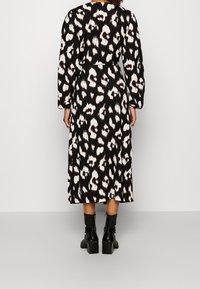 Svart klänning med leopardmönster i vitt och brunt, med långa ärmar, avslappnad passform och längd till mitten av vaden. Bärs tillsammans med svarta klackboots.