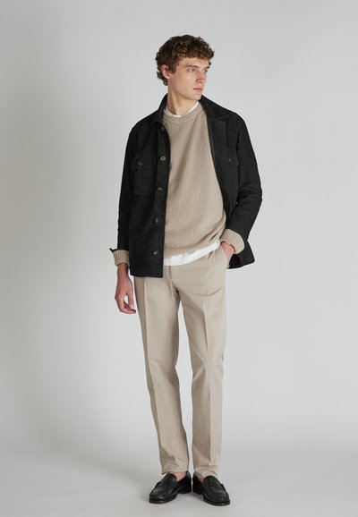 Giacca scura in suede con tasche frontali, maglione in knit beige, pantaloni beige e mocassini neri. Design semplice e strutturato con colori neutri.